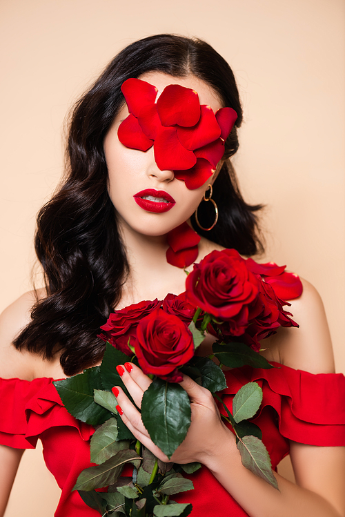 young woman with petals on face holding red roses isolated on pink