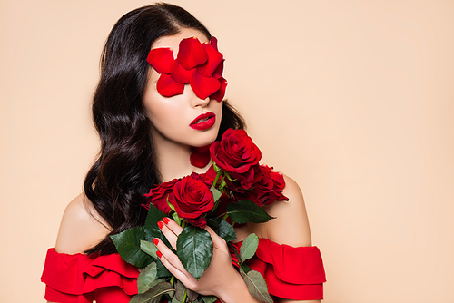 young brunette woman with petals on face holding red roses isolated on pink
