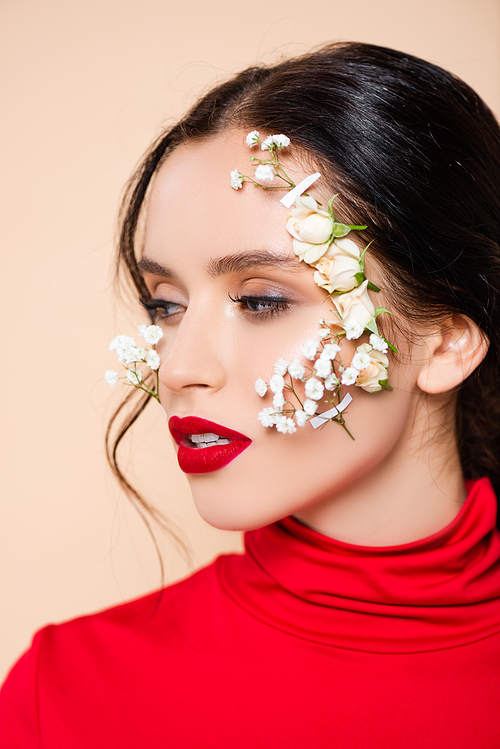 young woman with red lips and flowers on face looking away isolated on pink