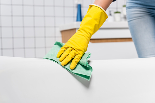 Cropped view of woman in rubber glove cleaning bathtub with rag in bathroom