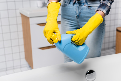 Cropped view of woman in rubber gloves opening bottle of cleaner near bathtub