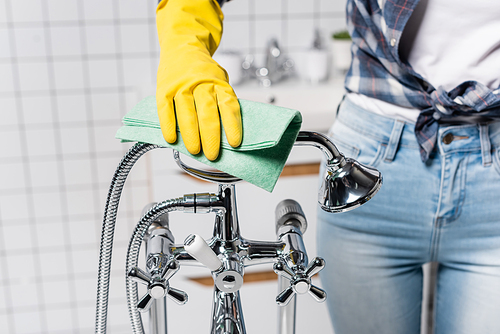 Cropped view of woman in rubber glove cleaning shower with rag in bathroom on blurred background