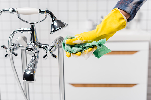 Cropped view of woman in rubber glove holding rag with soap near faucet and shower in bathroom