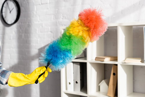 Cropped view of woman in yellow rubber glove holding colorful dust brush at home
