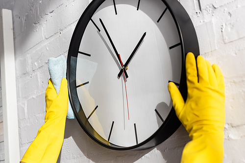 Cropped view of person in rubber gloves cleaning clock with rag on wall at home