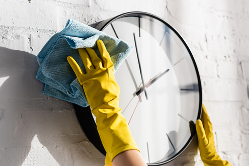 Cropped view of woman in rubber gloves cleansing wall clock with rag