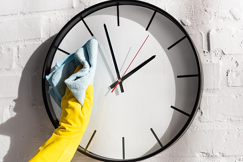Cropped view of person in rubber glove cleaning clock with rag on white brick wall