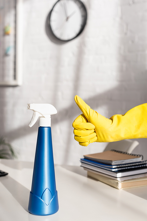 Cropped view of bottle of detergent and hand in rubber glove showing like gesture near table