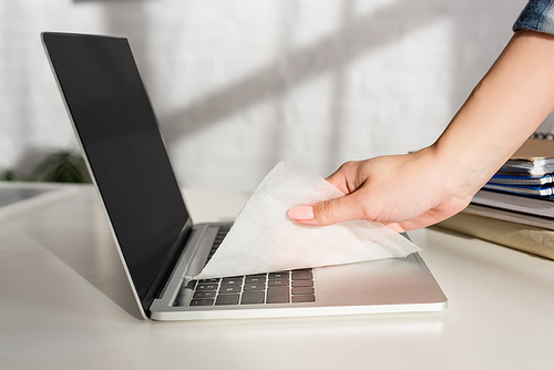Cropped view of woman cleaning laptop keyboard with napkin near notebooks on table