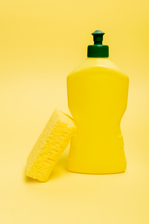 Sponge near bottle of dishwashing liquid on yellow background with copy space