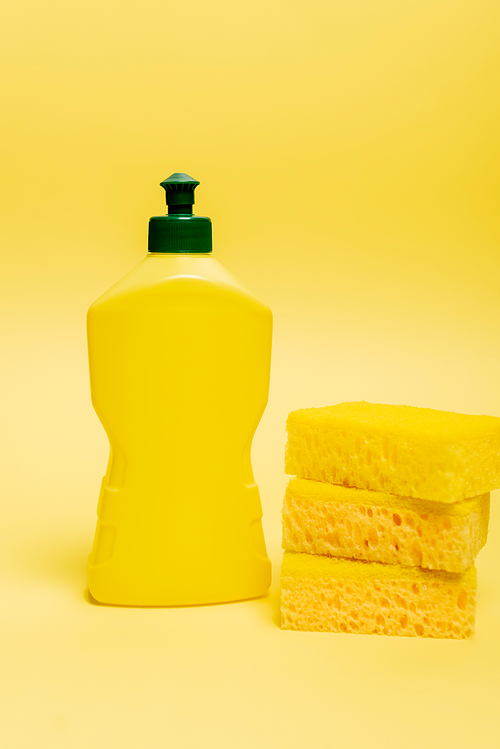Sponges and bottle of dishwashing liquid on yellow background