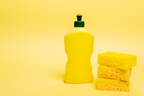 Yellow sponges and bottle of dishwashing liquid with cap on yellow background