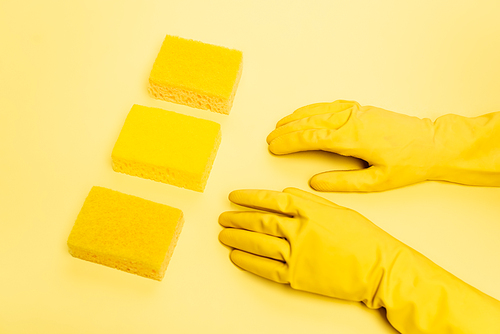 High angle view of person in rubber gloves and sponges on yellow background