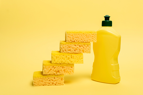 Sponges near yellow bottle of dishwashing liquid on yellow background