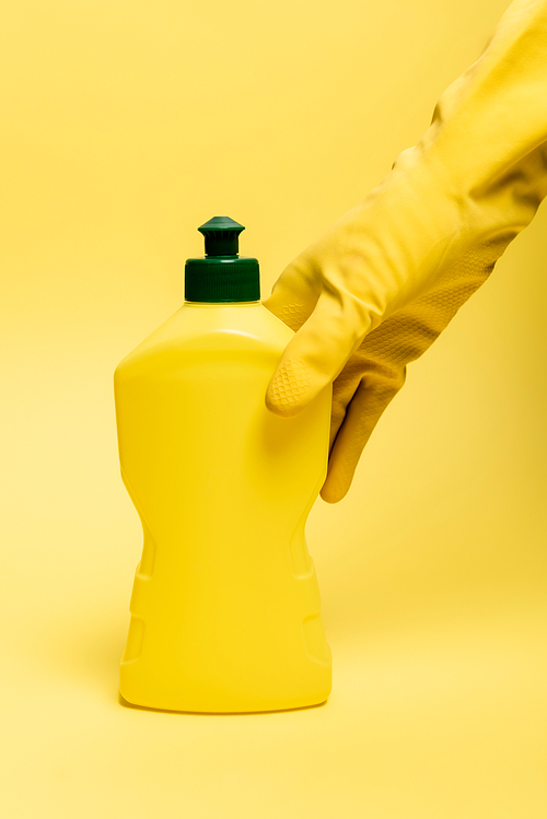 Cropped view of hand in rubber glove taking dishwashing liquid on yellow background