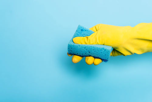 Cropped view of hand in rubber glove holding sponge on blue background