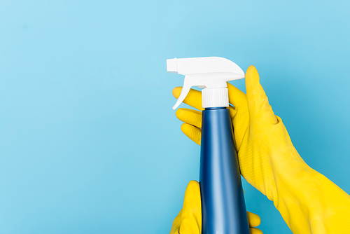 Cropped view of hands in yellow rubber gloves holding detergent with sprayer on blue background
