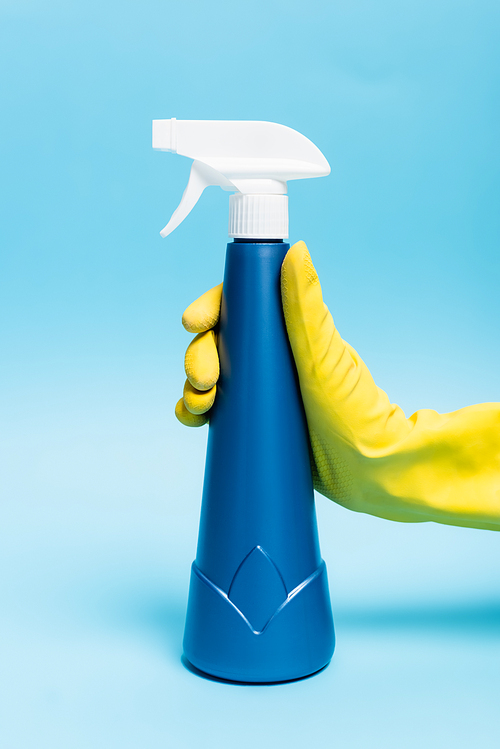 Hand in yellow rubber gloves holding detergent with sprayer on blue background