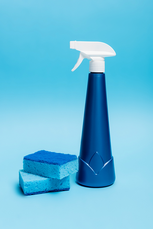 Blue bottle of detergent and sponges on blue background