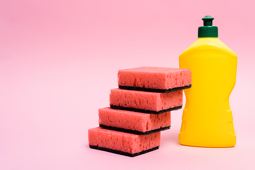 Pink sponges and bottle of dishwashing liquid on pink background
