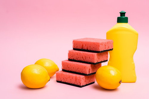 Fresh lemons near sponges and dishwashing liquid on pink background