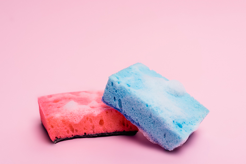 Colorful sponges with soapsuds on pink background
