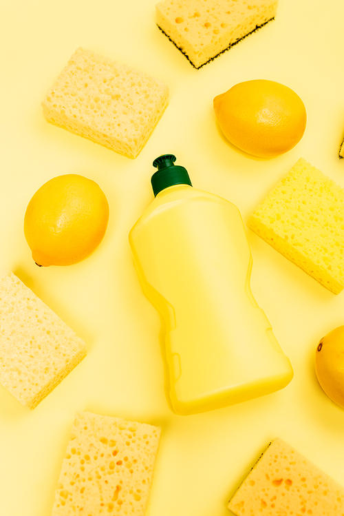 Top view of dishwashing liquid, sponges and lemons on yellow background
