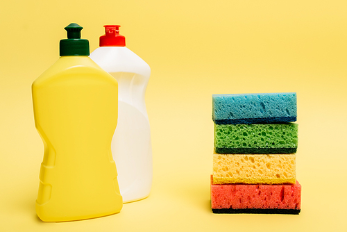 Bottles of dishwashing liquid and colorful sponges on yellow background