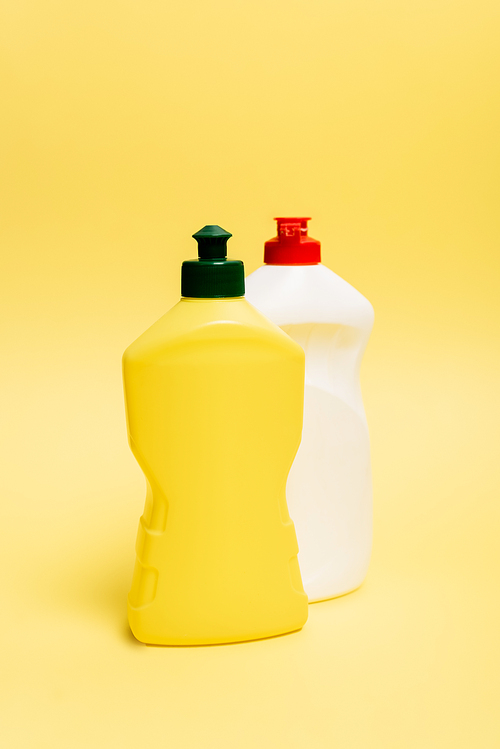Bottles of dishwashing liquid on yellow background