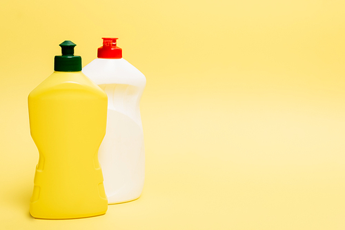 Bottles of dishwashing liquid on yellow background with copy space