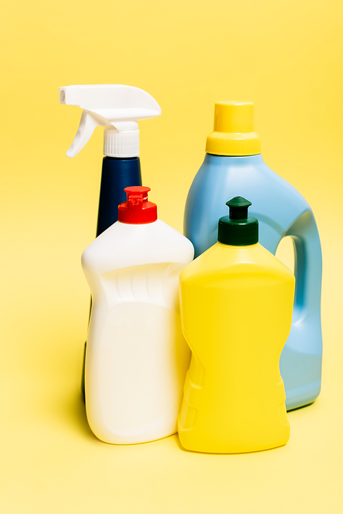 Bottles of dishwashing liquid and detergents on yellow background