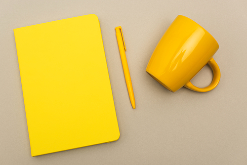 top view of yellow notebook near pen and empty mug isolated on grey