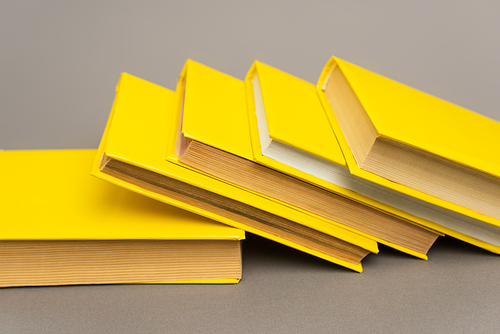 stacked yellow notebooks and books on grey