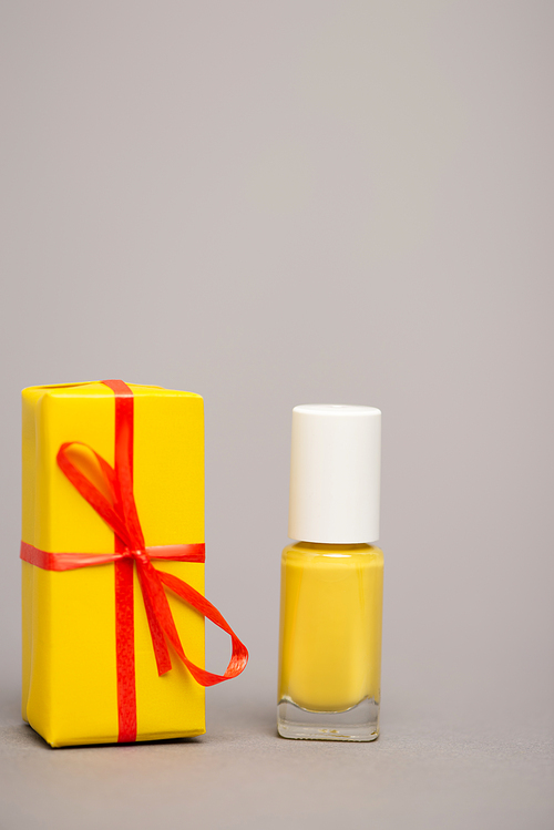 wrapped yellow gift box near bottle with nail polish isolated on grey