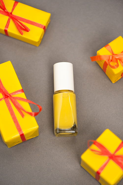 high angle view of wrapped gift boxes near bottle with yellow nail polish on grey