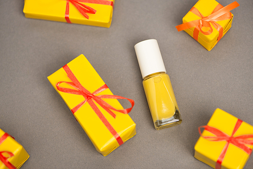 high angle view of wrapped yellow gift boxes near bottle with nail polish on grey