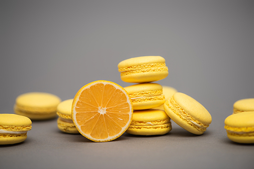 delicious yellow macarons near half of juicy lemon on grey background