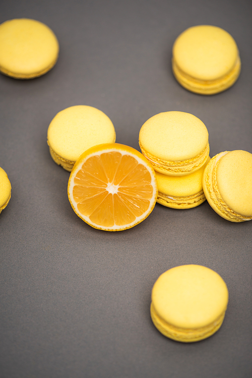 high angle view of delicious yellow macarons near half of juicy lemon on grey background