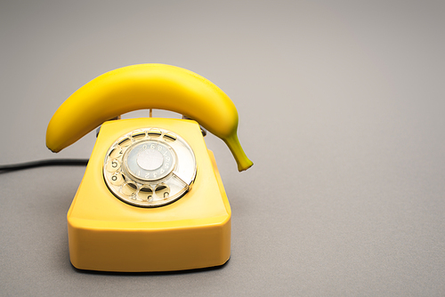 yellow banana on retro telephone on grey background