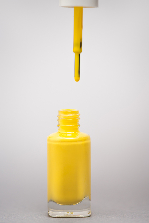 bottle with yellow nail polish and brush on grey background