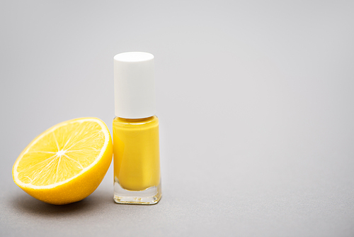 bottle with yellow nail polish and half of lemon on grey background
