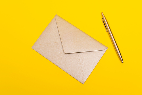 top view of envelope near golden pen isolated on yellow