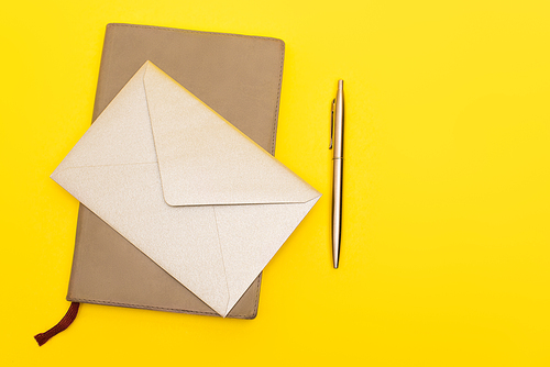 top view of envelope on notebook near pen isolated on yellow