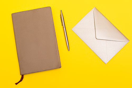top view of envelope near copy book and golden pen isolated on yellow