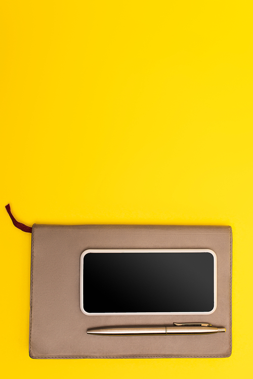 top view of mobile phone with blank screen on copy book with golden pen isolated on yellow