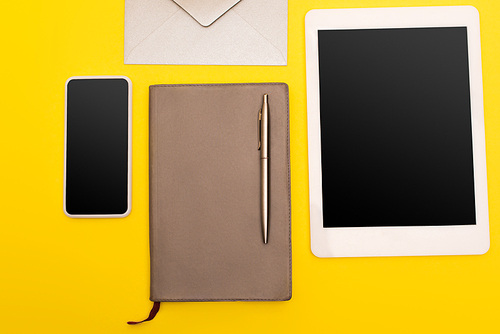 top view of gadgets with blank screen near copy book with golden pen near envelope  isolated on yellow