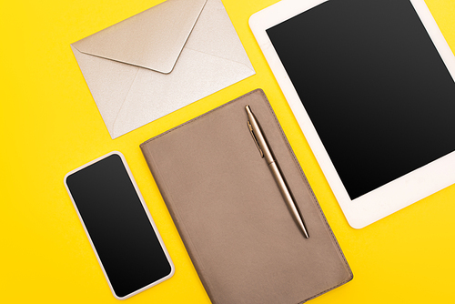top view of devices with blank screen near copy book with golden pen near envelope  isolated on yellow