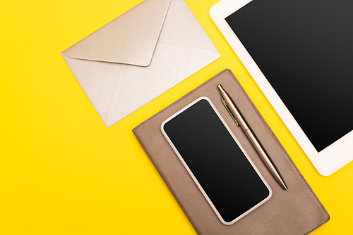 top view of devices with blank screen near notebook with golden pen near envelope  isolated on yellow