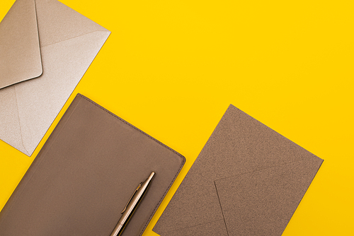 top view of notebook with golden pen near envelopes isolated on yellow