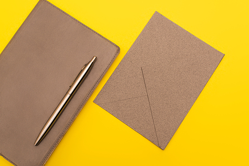 top view of notebook with golden pen near paper envelope isolated on yellow